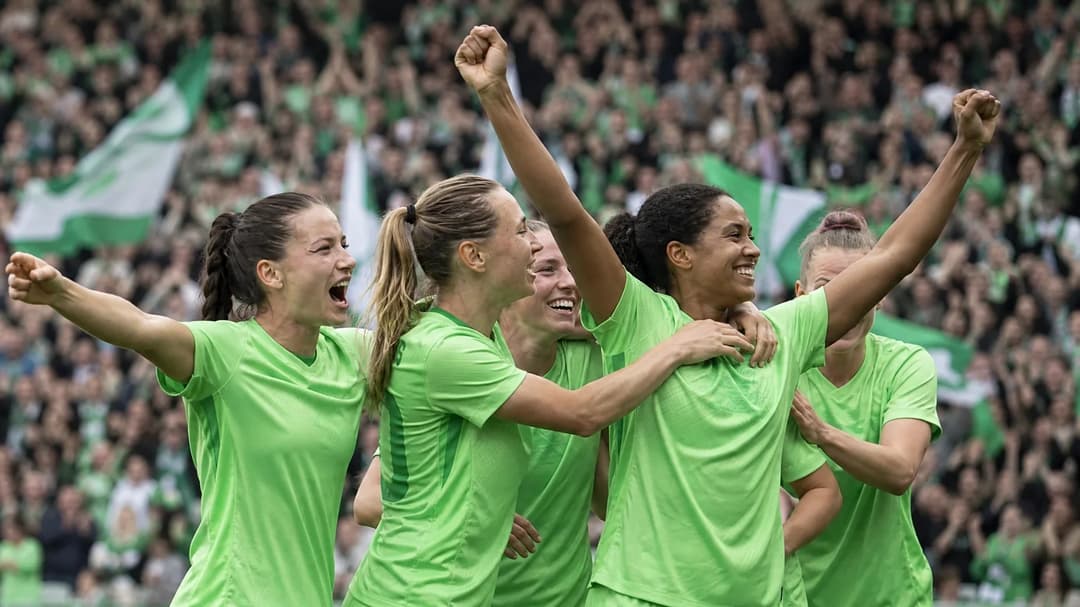 Wolfsburg players celebrating a goal with ecstatic fans in the background.