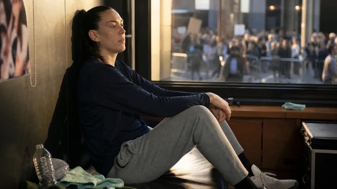 Breanna Stewart sitting thoughtfully in a dimly lit players' lounge, gazing out a window while dressed in sports attire.