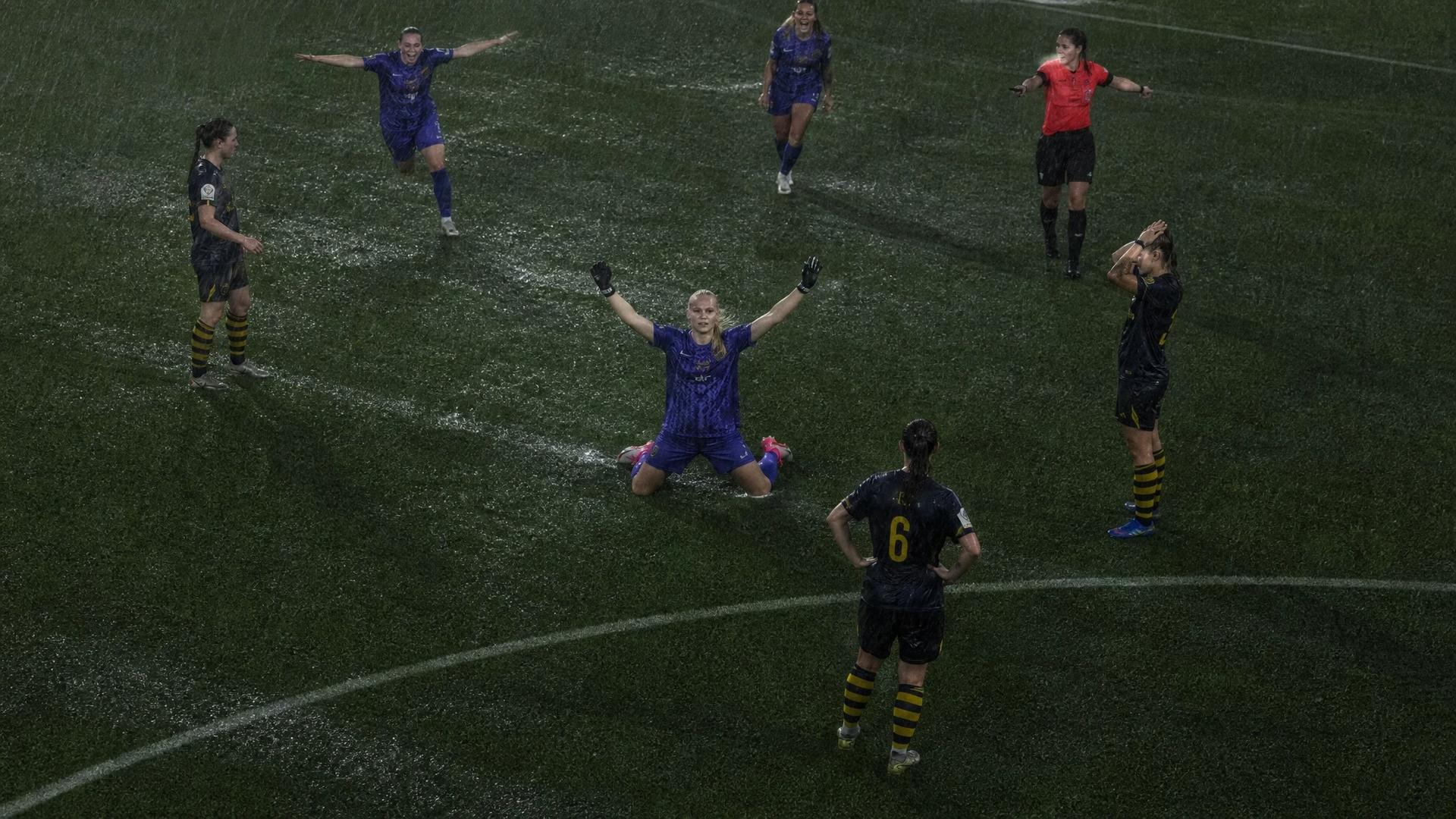 A bird's-eye view of a football pitch in heavy rain with players celebrating and the match being halted.