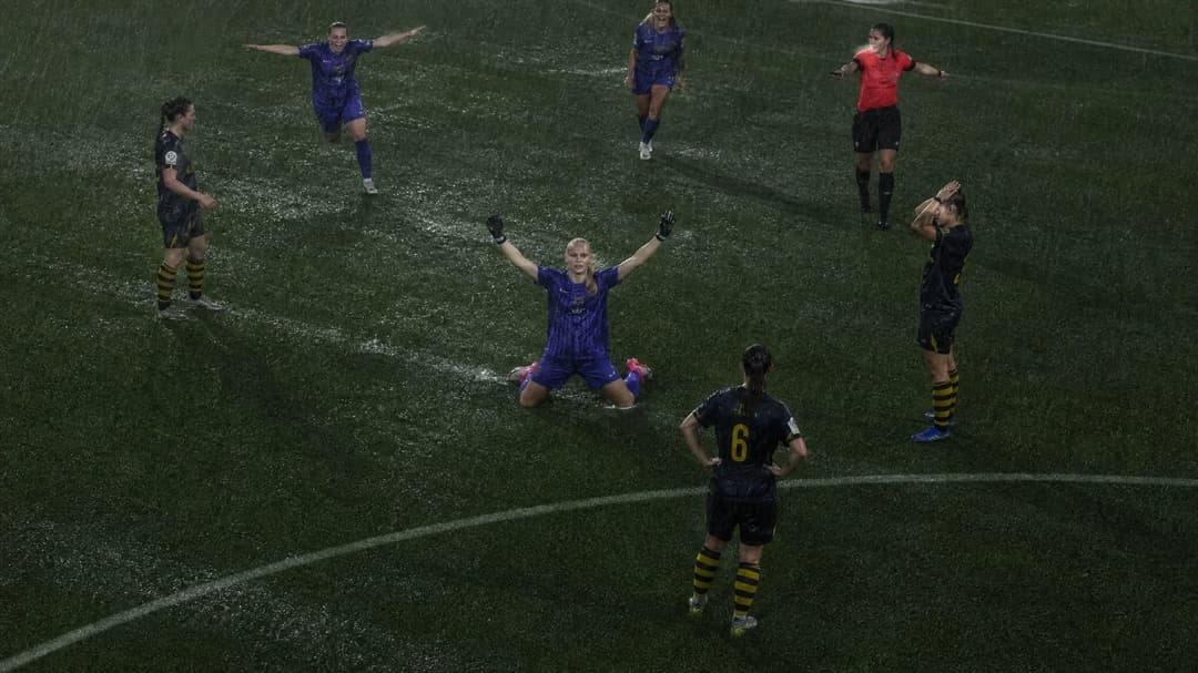 A bird's-eye view of a football pitch in heavy rain with players celebrating and the match being halted.