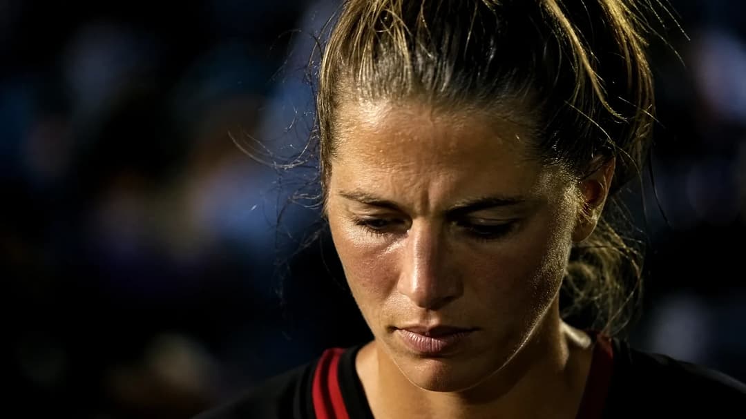 Close-up of a female football player in a quiet reflective moment, illuminated by a single spotlight.