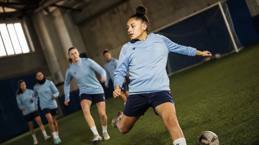 A female football player strikes a ball in a training facility.