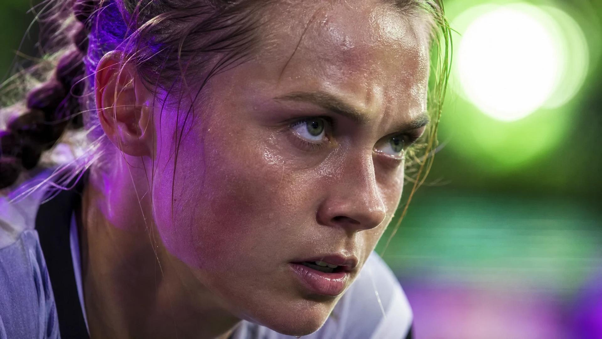 An extreme close-up of a focused female football player from 1. FC Köln during a match, with neon lighting highlighting her intense expression.
