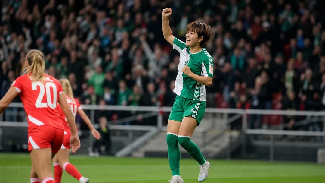 A female football player celebrating a goal amid a cheering crowd in a stadium.