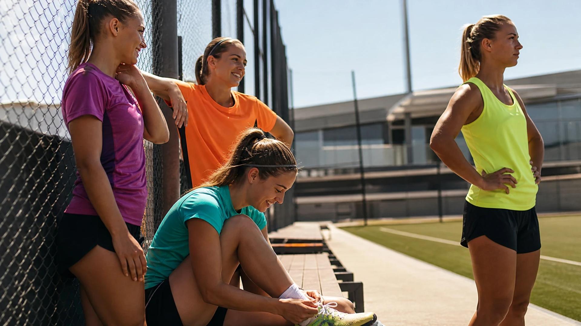 Four young female footballers relaxing during a training break in a sunlit facility.