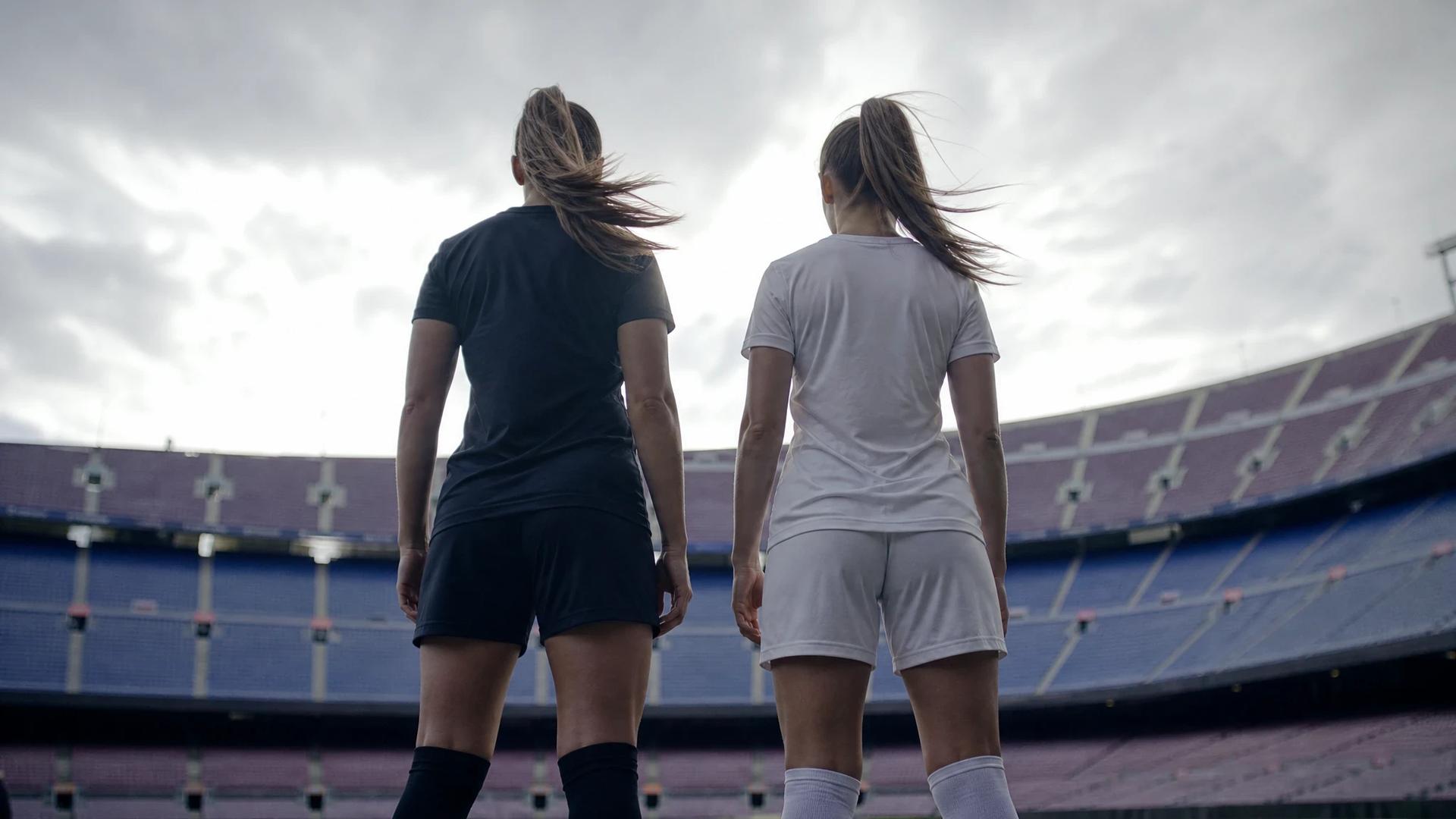 Two female football players silhouetted against a bright background, preparing for a match.