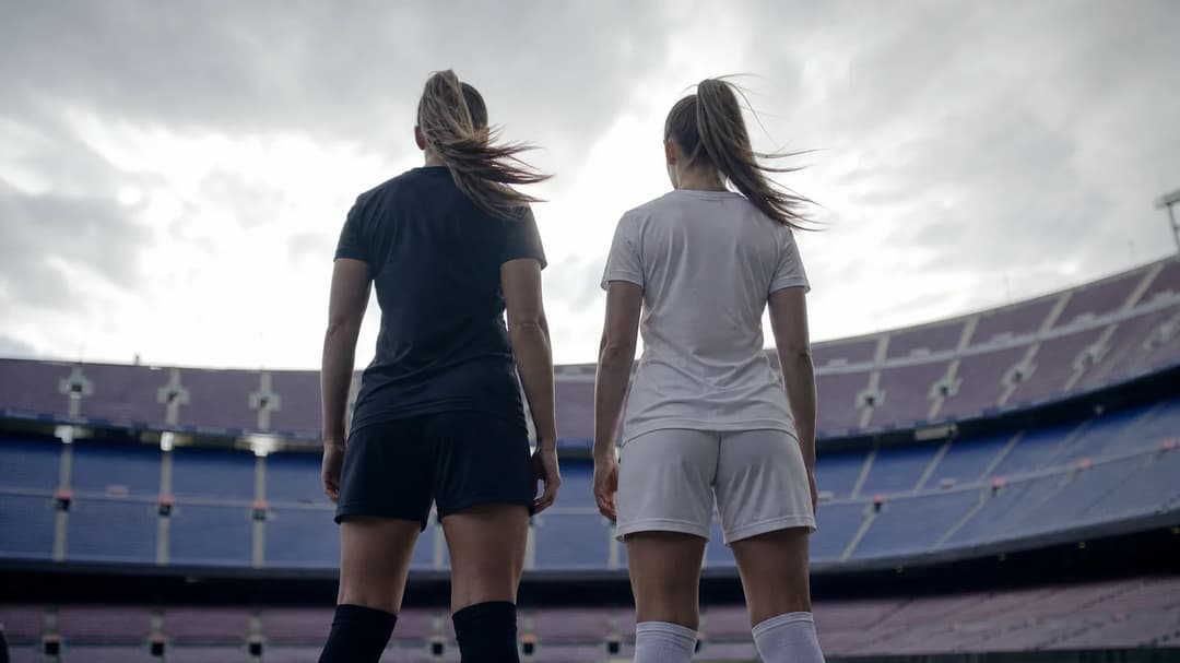 Two female football players silhouetted against a bright background, preparing for a match.