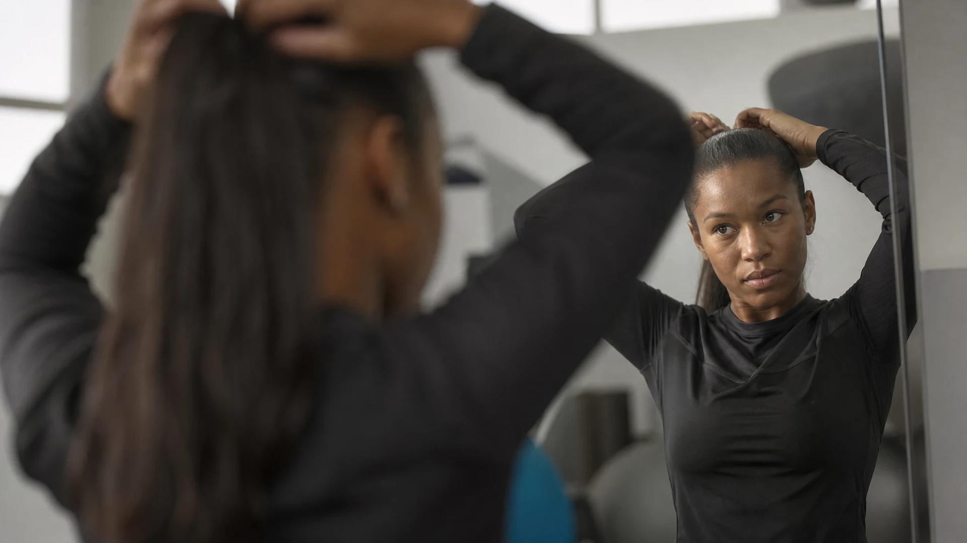 A female football player adjusting her hair in front of a mirror during a training session.
