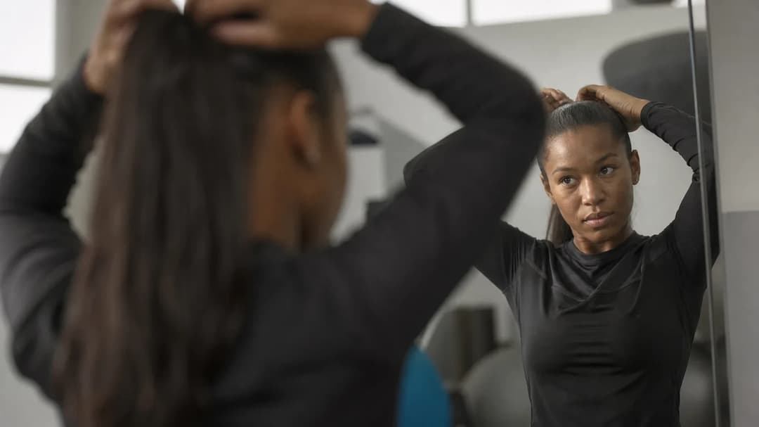 A female football player adjusting her hair in front of a mirror during a training session.
