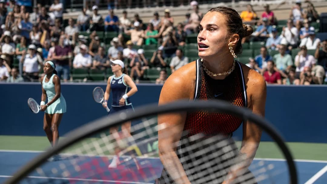 A tense scene at the US Open with Aryna Sabalenka practicing her serve while fans watch intently.