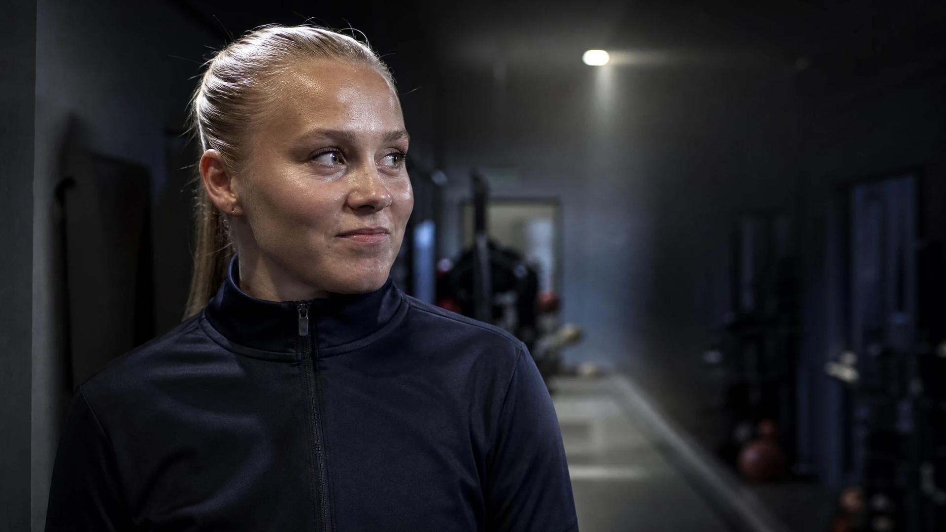 Emilie Libakken Österås in a training facility hallway, looking contemplative.