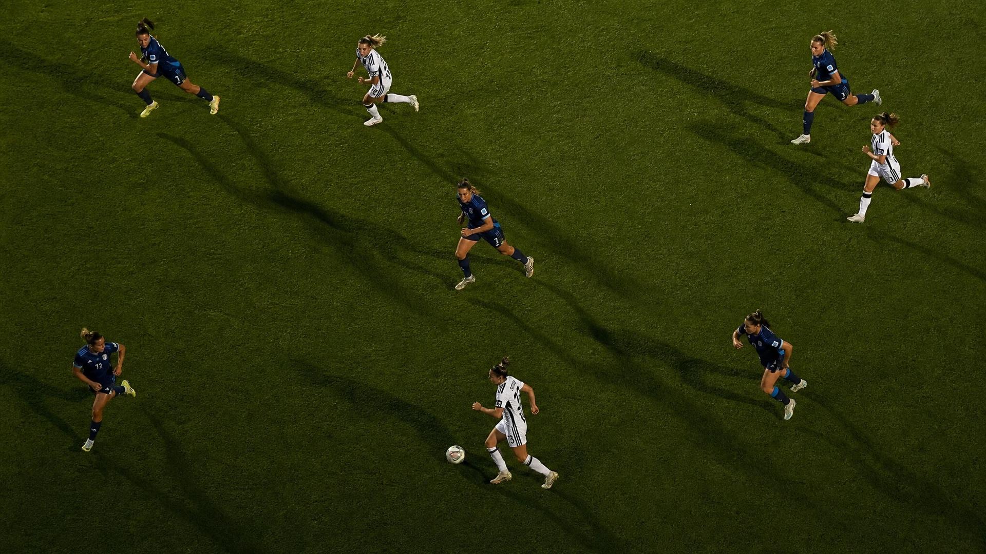 Bird's-eye view of Juventus Women players in action on a football pitch, illuminated by dramatic lighting.