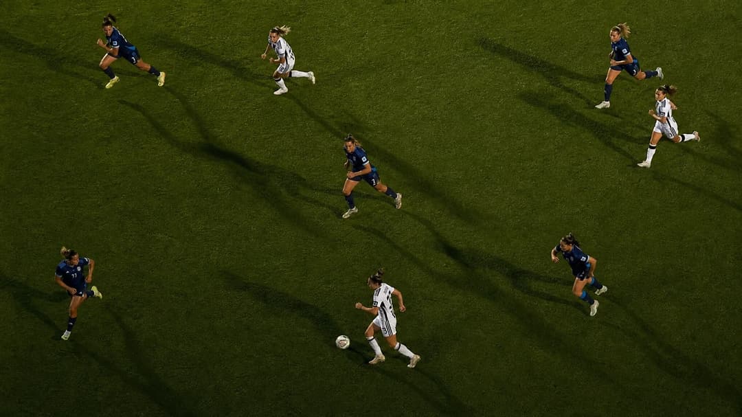 Bird's-eye view of Juventus Women players in action on a football pitch, illuminated by dramatic lighting.