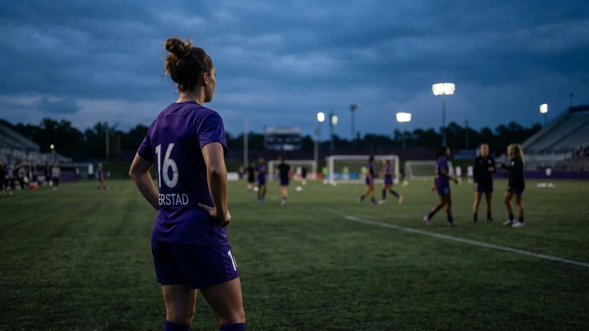 A female footballer from the Orlando Pride is shown in an over-the-shoulder shot, illuminated by dusk light on a football pitch.