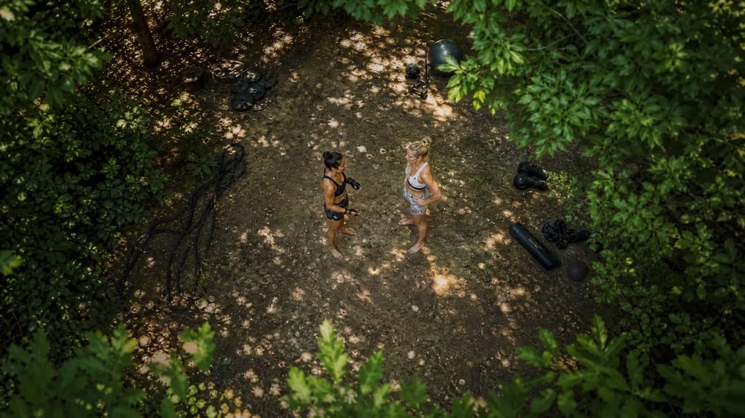 Two female coaches discussing in an open training area surrounded by greenery.