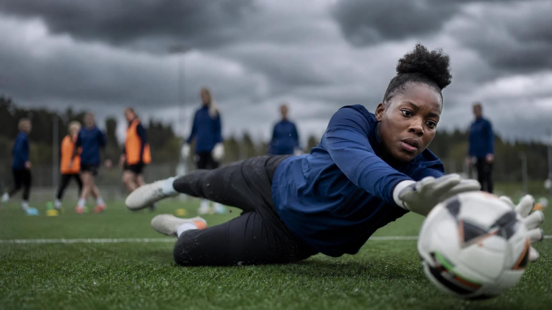 A goalkeeper named Comfort Erhabor dives during a training session with AIK while other players practice in the background.