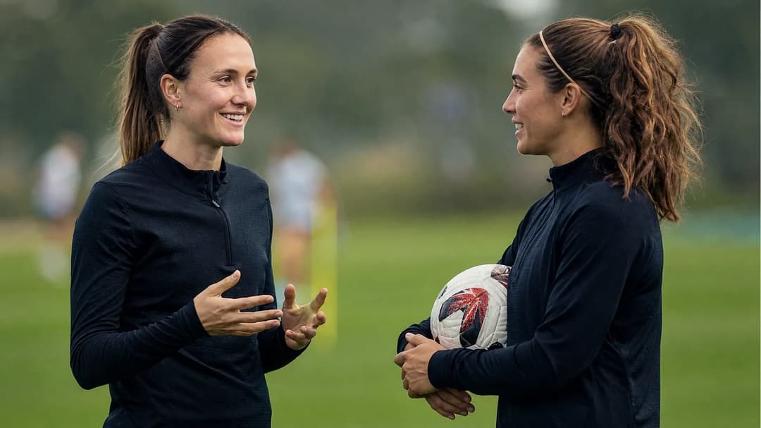 Lotte Wubben-Moy and Mariona Caldentey sharing a conversation on a training pitch.