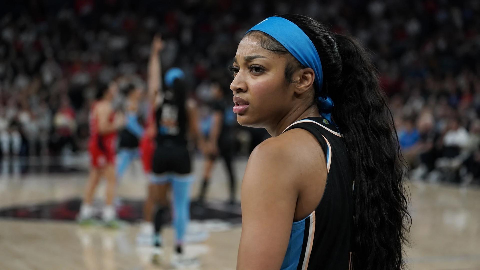 A tense moment capturing Angel Reese on the basketball court after receiving a technical foul, with blurred teammates celebrating in the background.