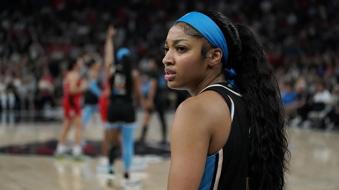 A tense moment capturing Angel Reese on the basketball court after receiving a technical foul, with blurred teammates celebrating in the background.