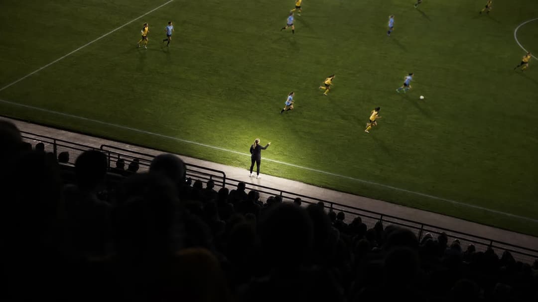 A bird's-eye view of a football match showing a female coach directing her team, capturing a dynamic moment of play.