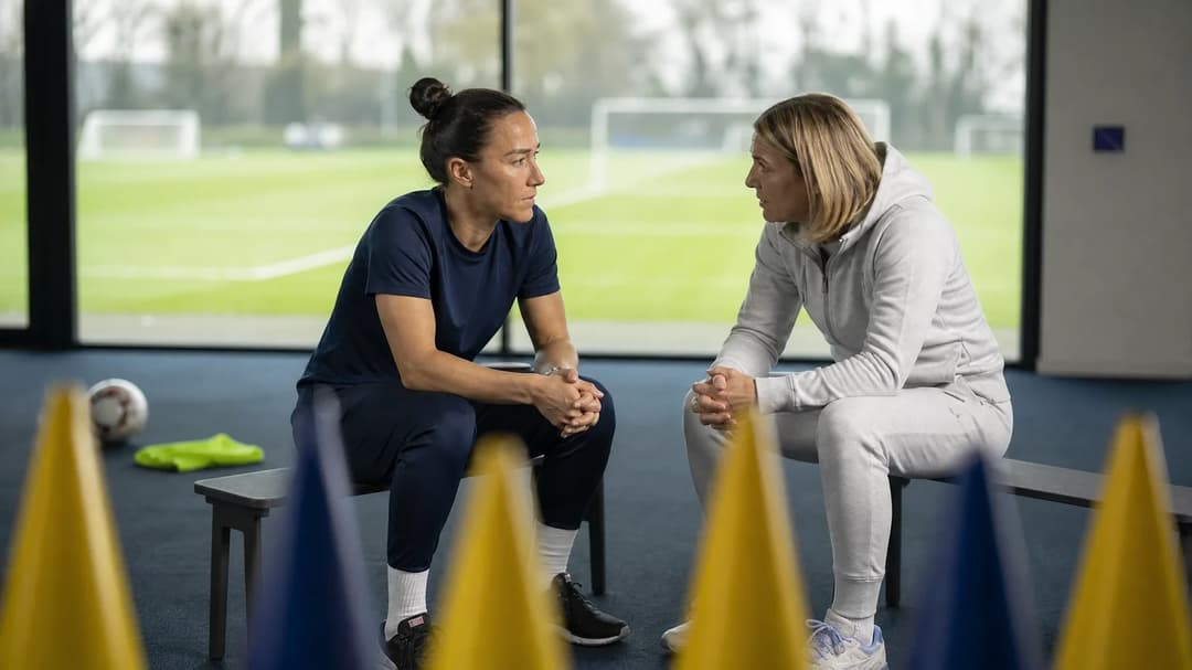 Lucy Bronze and Sonia Bompastor engaged in conversation inside a training facility.