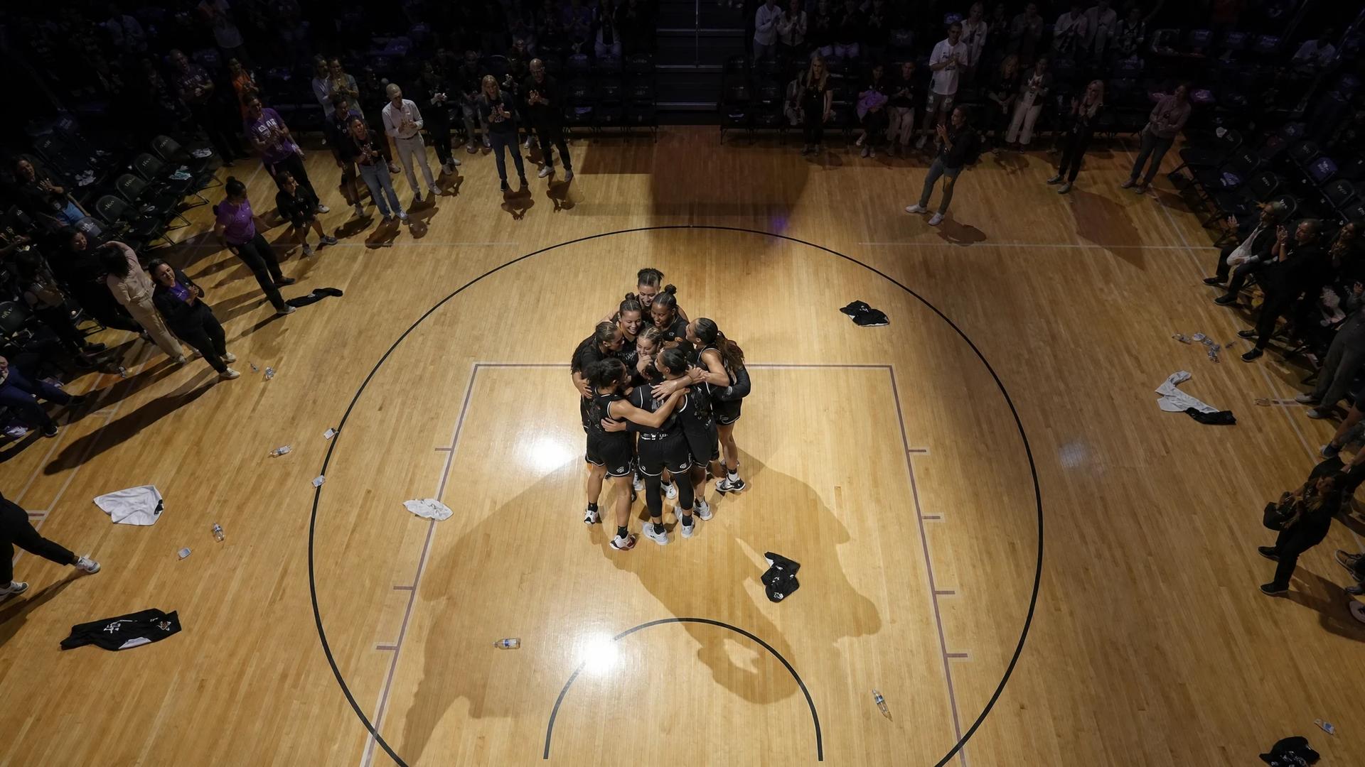 A bird's-eye view of players celebrating in a basketball arena after a game.