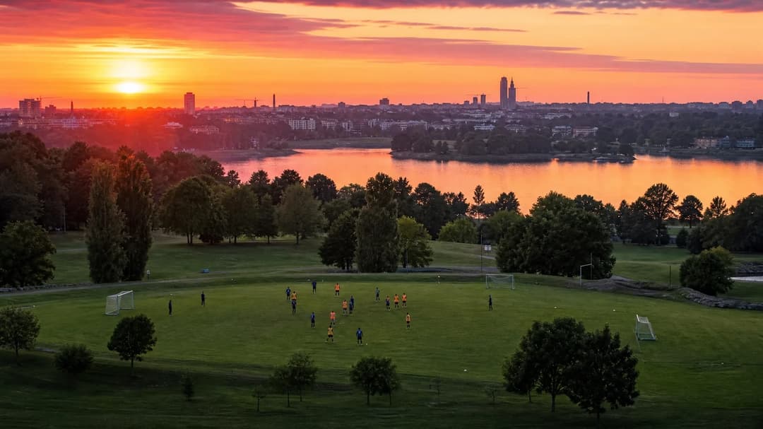 A panoramic view of a football pitch during golden hour with female players practicing in the distance.