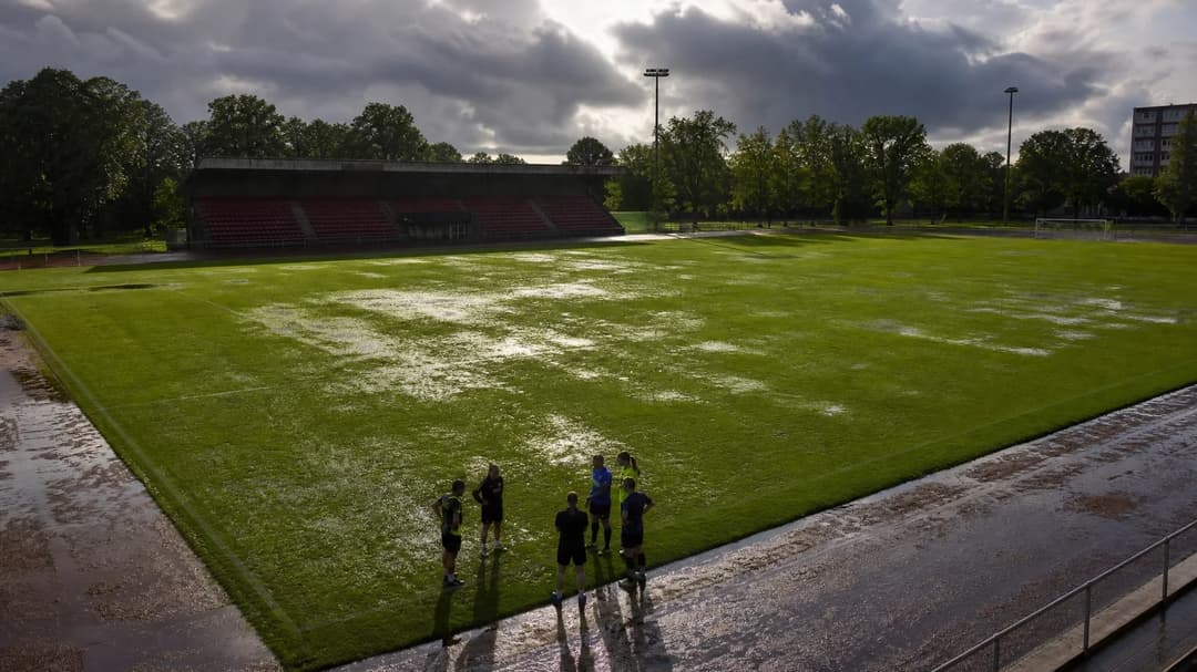 Wide shot of a rain-soaked football pitch at Skytteholms IP with players on the sidelines.