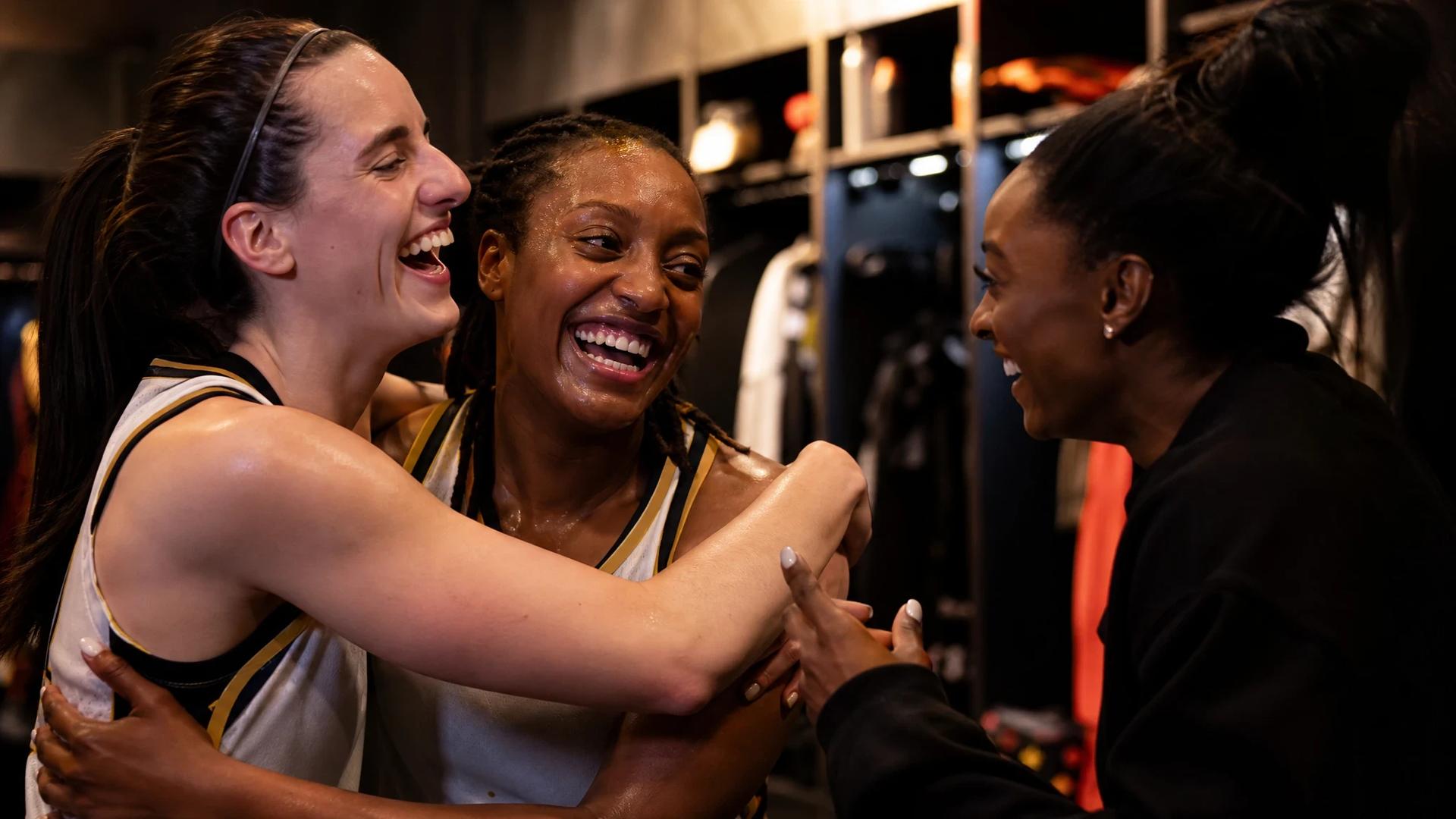 Caitlin Clark and Kelsey Mitchell celebrate in the locker room, while Simone Biles interacts with them.