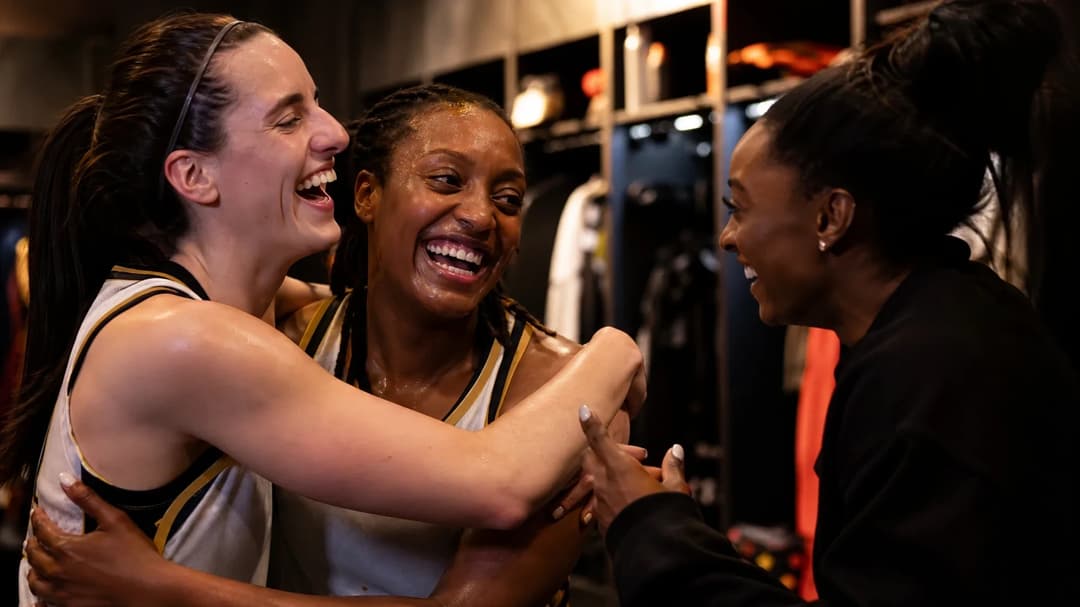 Caitlin Clark and Kelsey Mitchell celebrate in the locker room, while Simone Biles interacts with them.