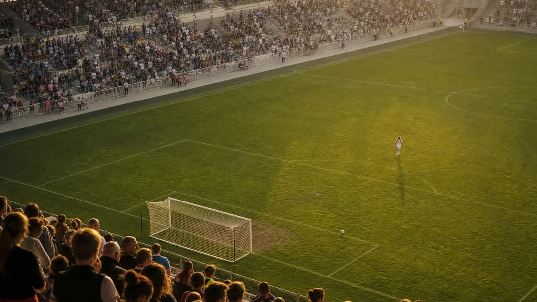 An aerial view of an empty football stadium with scattered fans leaving after a match.