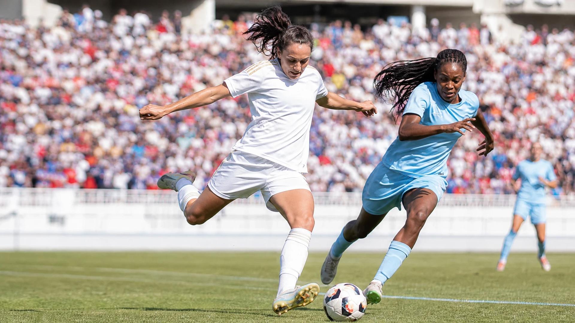 Two female football players in action on a sunny day in a stadium.