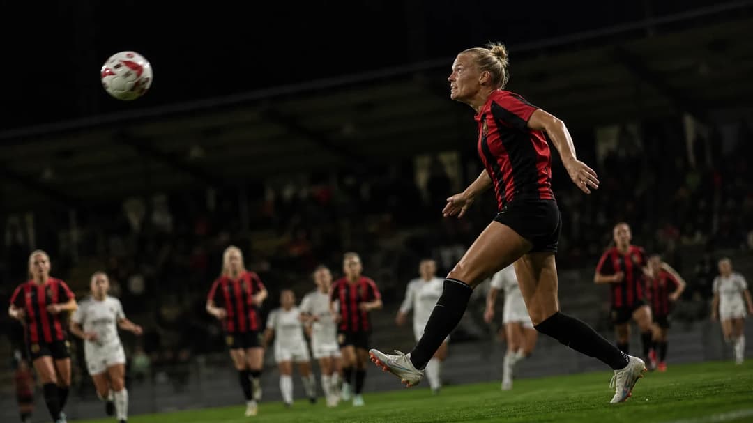 A female football player poised to jump for a cross during a tense moment in a match.