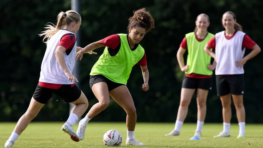 A group of female football players in colorful sports gear practicing on a sunny training ground.