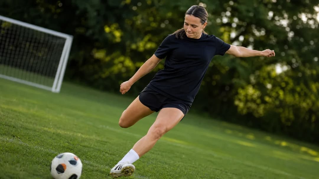 A footballer in mid-action, striking the ball during a training session on a sunny day.