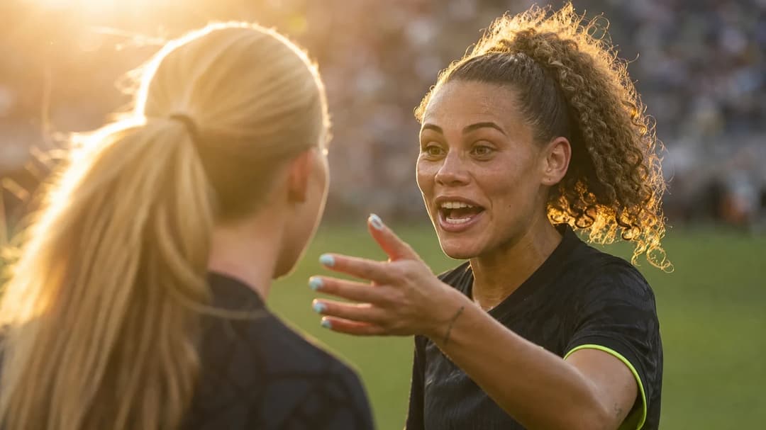 Paige Metayer and Trinity Rodman share a moment of celebration on the football pitch during golden hour.
