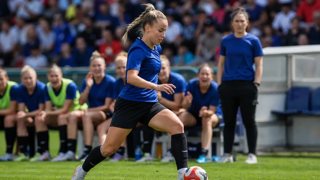 Female football player Giulia Gwinn in action on the pitch, surrounded by teammates under bright sunlight.