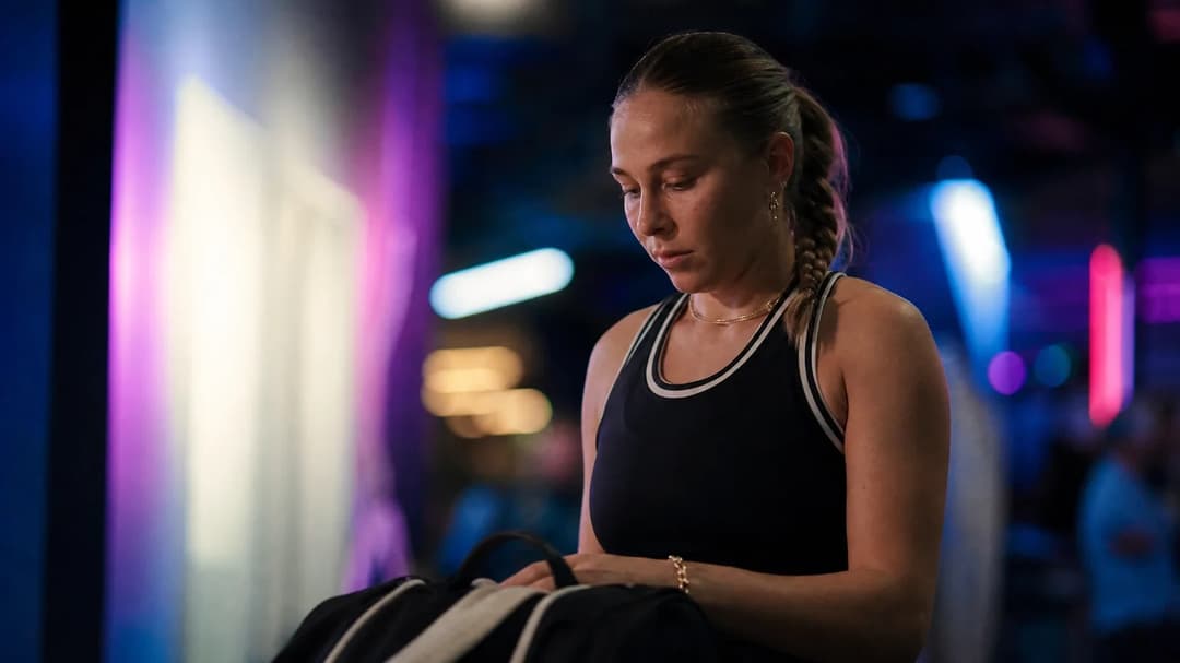 Amanda Anisimova stands beside her tennis bag in a quiet moment away from the action at the US Open, illuminated by neon lights.