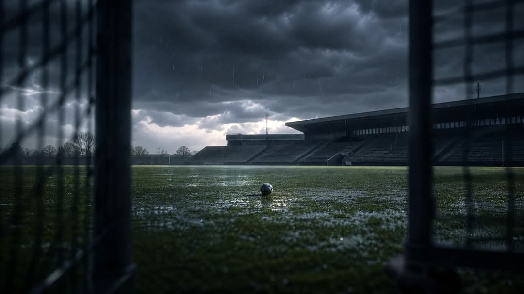 A deserted football pitch at dusk with stormy clouds overhead and a football on the ground.