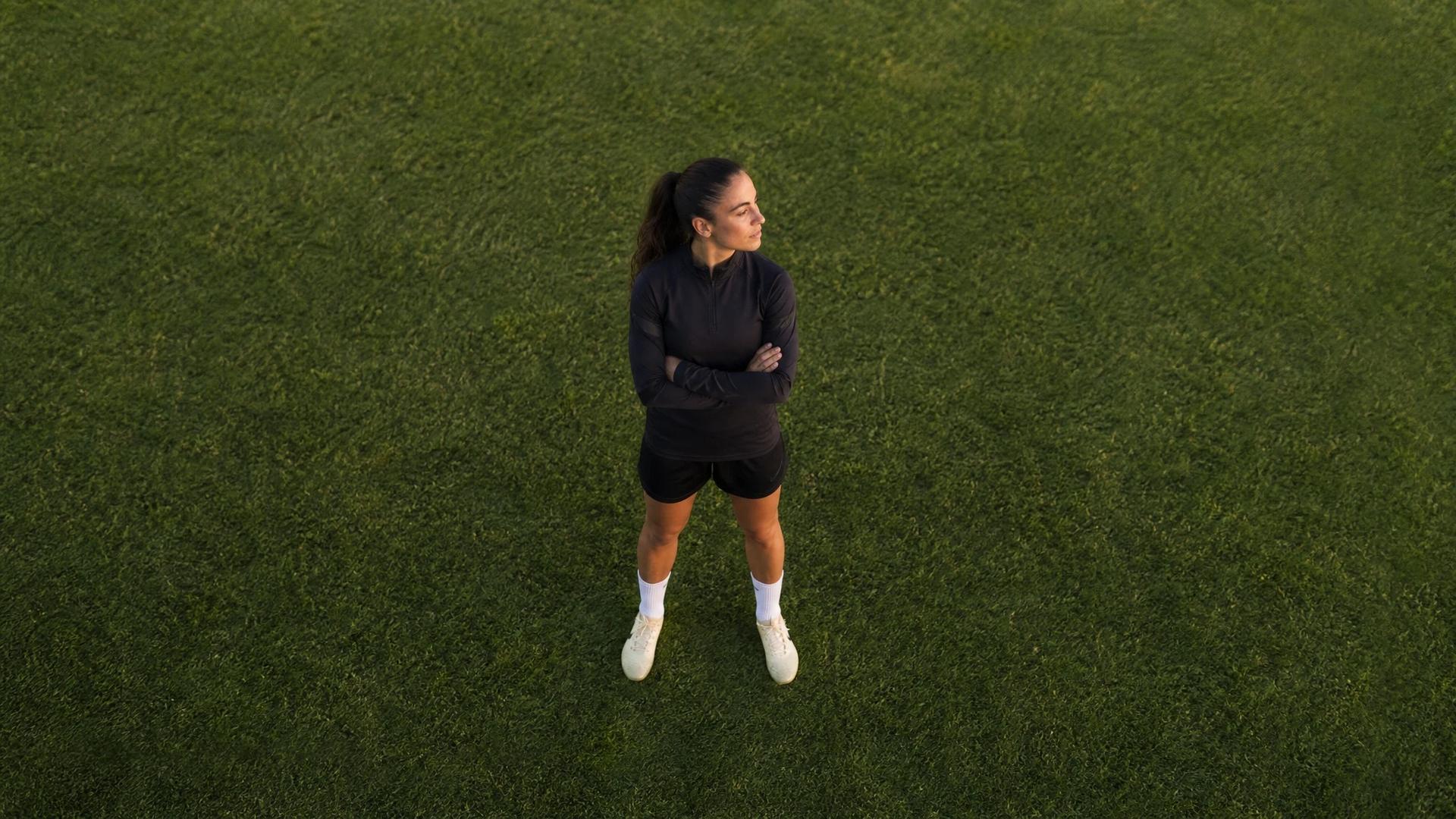 Aerial view of a female football player standing on a pitch, reflecting.