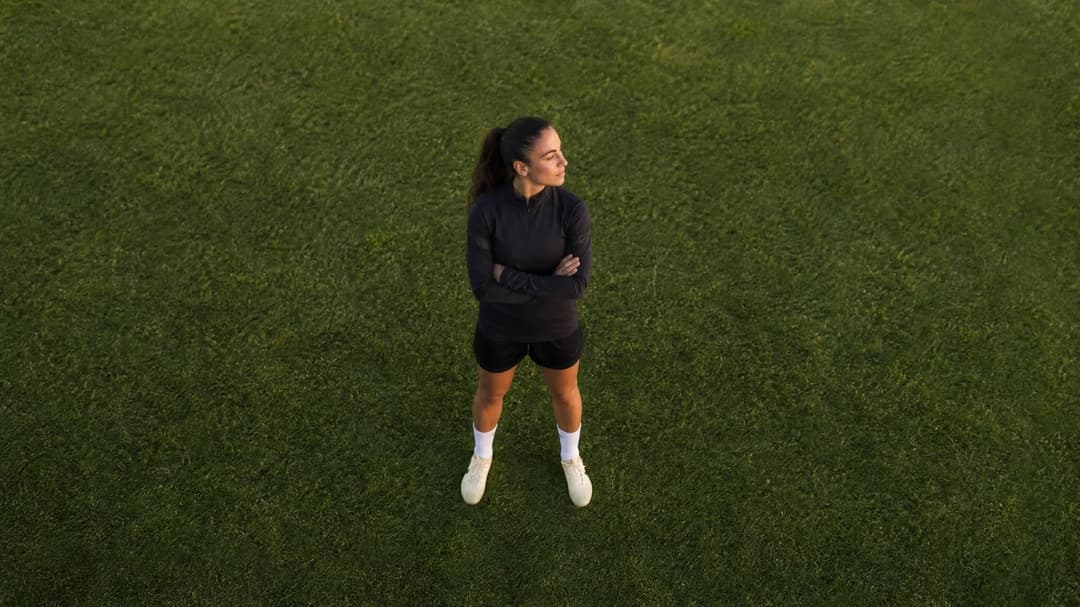 Aerial view of a female football player standing on a pitch, reflecting.