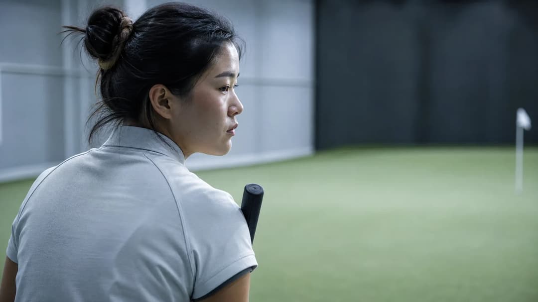 A female golfer stands with a putter in a practice green, gazing contemplatively at the space ahead.