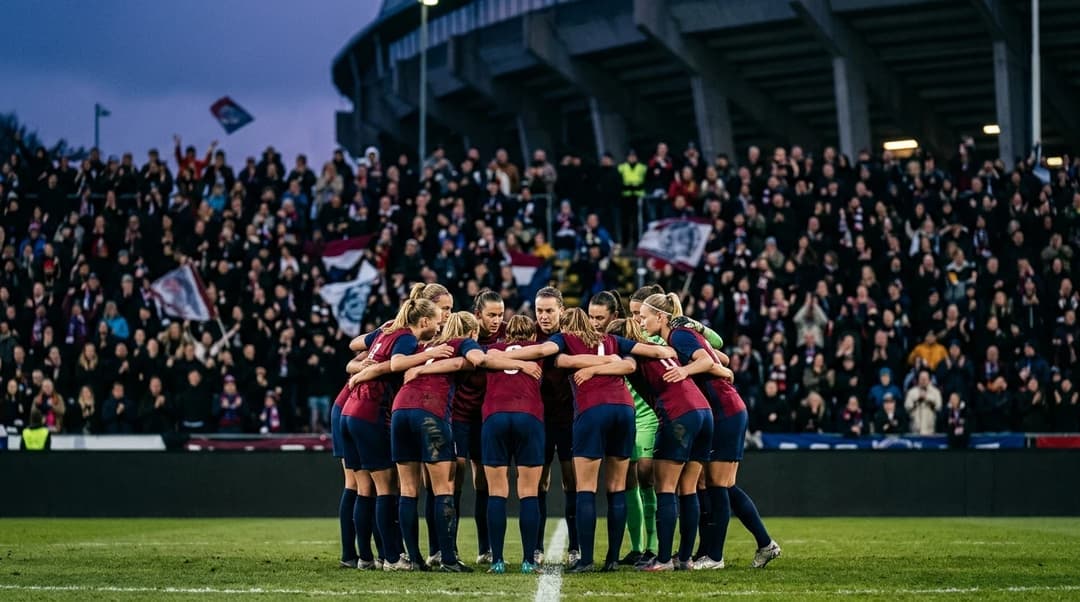 Vittsjö players huddled together in a stadium before a match, surrounded by cheering fans in the fading light.