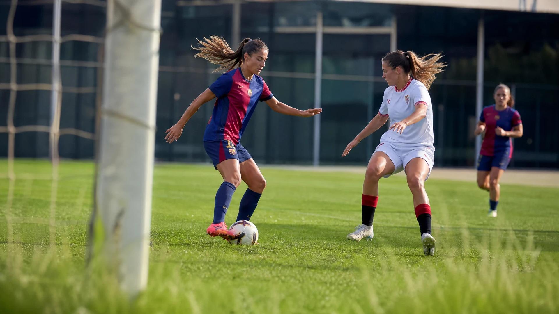 Two female football players training on a pitch, one dribbling the ball and the other defending.