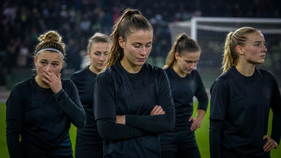 A group of female football players from VfL Wolfsburg standing on the pitch, looking disappointed.