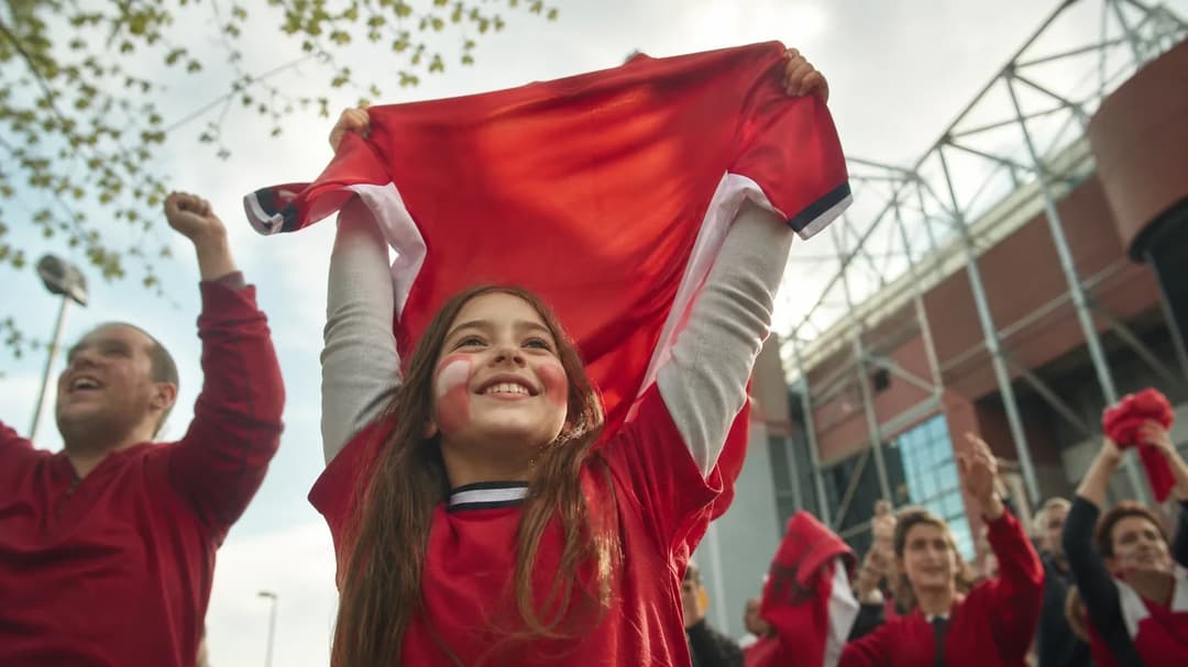A young fan celebrates outside Old Trafford with a Manchester United jersey, capturing the excitement of the club's new signing.