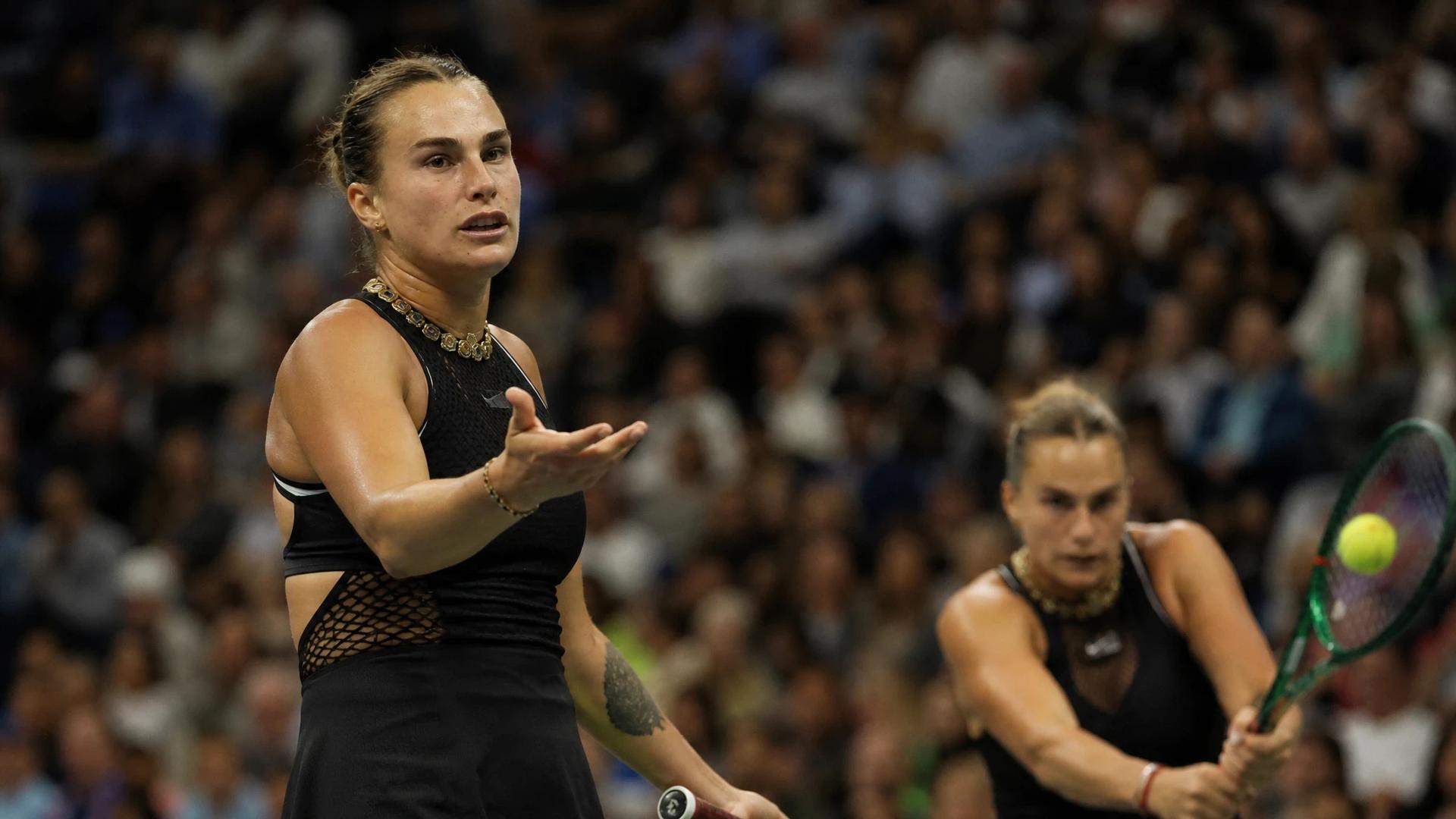 Aryna Sabalenka gestures towards the umpire during her match, with Kamilla Rakhimova in the background.
