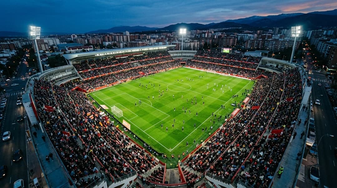 Aerial view of a football stadium during dusk with players warming up on the pitch.