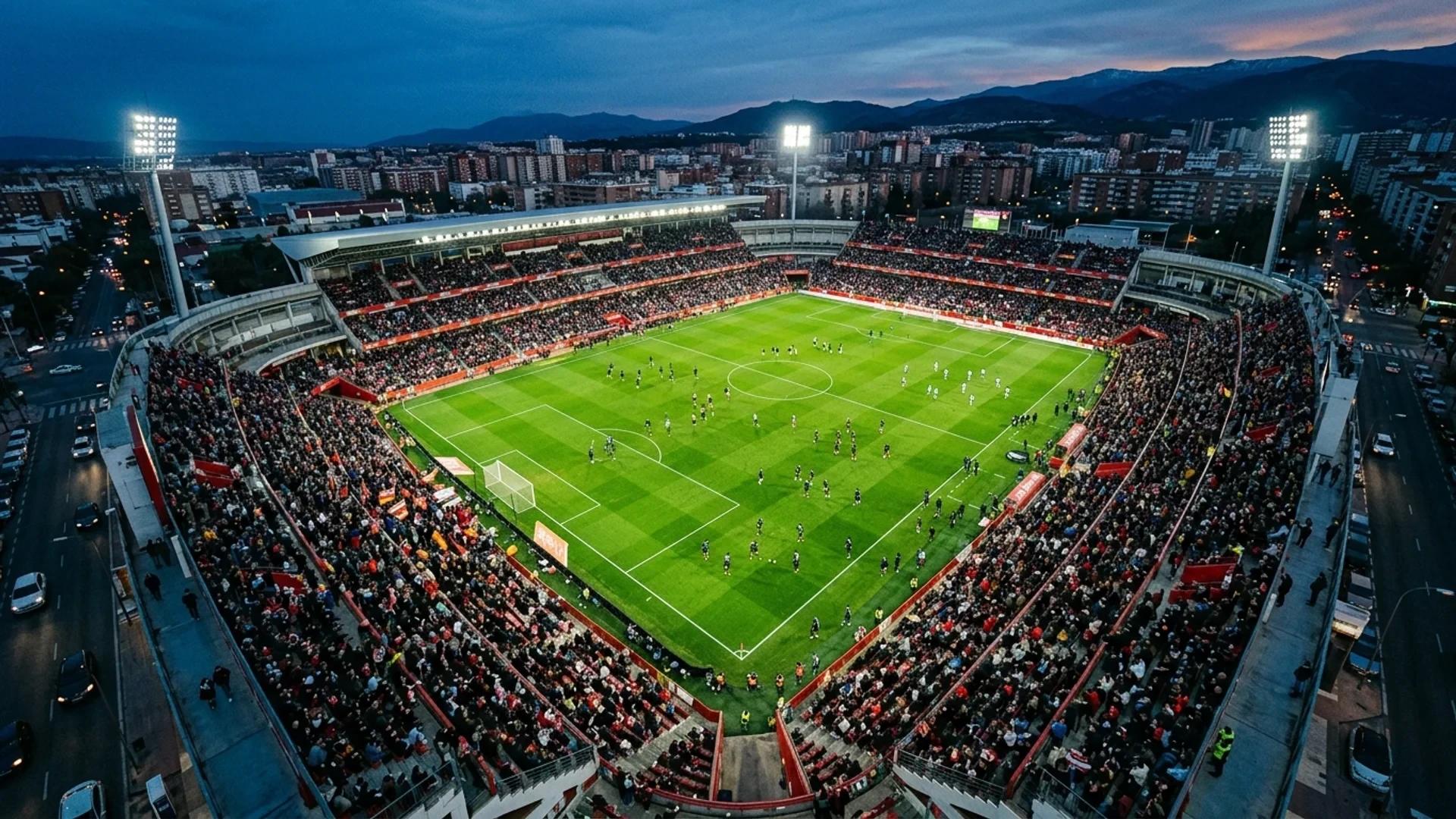 Aerial view of a football stadium during dusk with players warming up on the pitch.