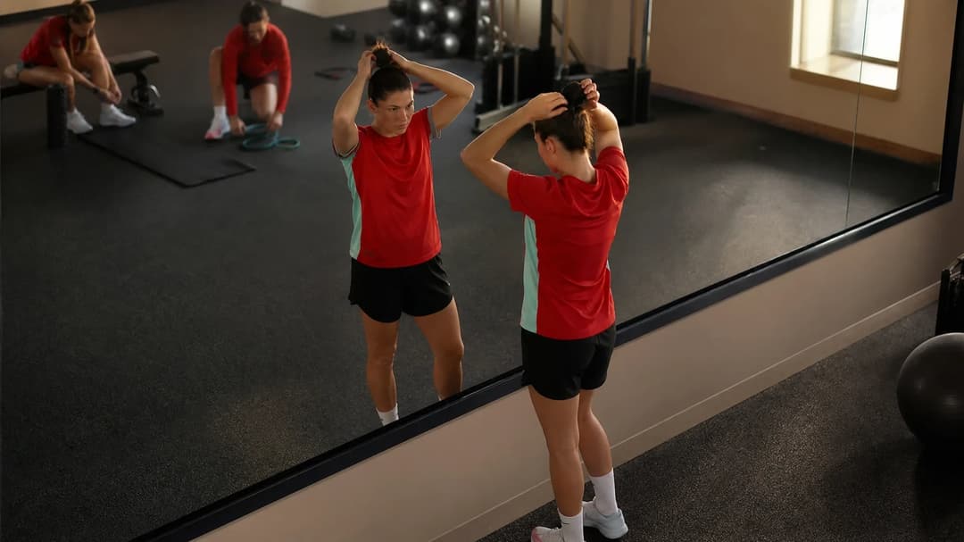 A female football player adjusting her hair in a training room, preparing for a match.